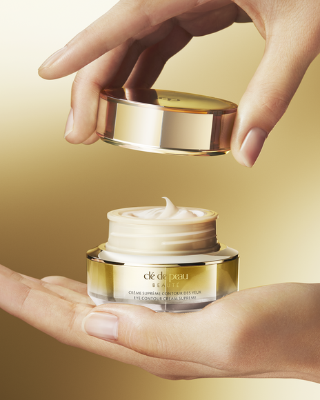 Photo of "EYE CONTOUR CREAM SUPREME" held in one hand with the lid being lifted.