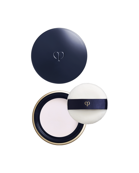 Photo of a round, blue-black and gold container with the lid placed above, showing the powder inside the main body below. On the right side, there is a white puff with a ribbon band and brand logo. Shade: Light.