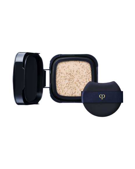 Photo of a "RADIANT CUSHION FOUNDATION DEWY (Refill)" refill case. Accompanied by a round navy puff with a gold logo. SHADE: I10
