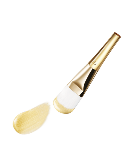 Photo of a gold-handled brush with white bristles, coated in the "PRECIOUS GOLD VITALITY MASK". 