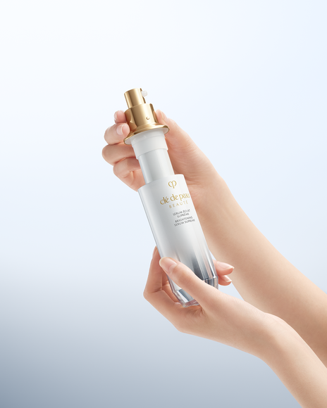 Photo of hands presenting a brightening serum bottle with the pump exposed.