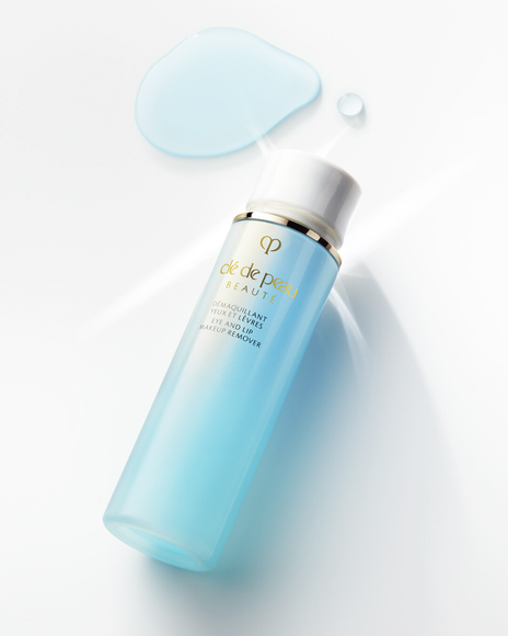 Photo of a bottle of "EYE AND LIP MAKEUP REMOVER M" next to pale blue liquid droplets spreading like water.