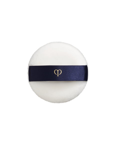Photo of a soft, round and white "PUFF (TRANSLUCENT LOOSE POWDER)". It has a blue-black ribbon handle engraved with the gold brand-logo.