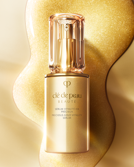 Photo of a visual of the "PRECIOUS GOLD VITALITY SERUM" bottle beautifully arranged against a backdrop wrapped in golden light. The glossy gold container and translucent cap evoke a luxurious atmosphere.