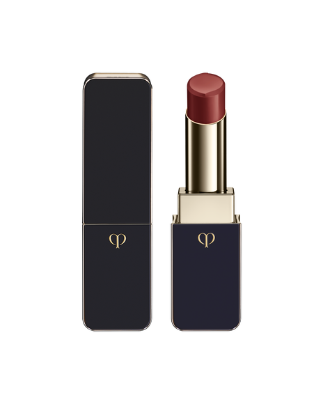 Photo of LIPSTICK SHINE with the bullet twisted up; the body combines blue‑black and gold sides with a gold emblem. SHADE: Canna Lily.
