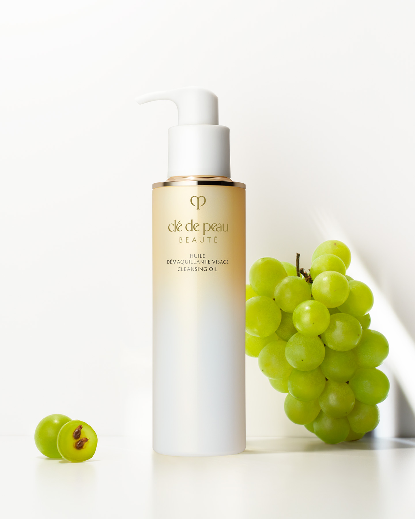 Photo of Cl&eacute; de Peau Beaut&eacute; CLEANSING OIL shown with a bunch of fresh grapes to emphasize the grape seed oil in the formula.