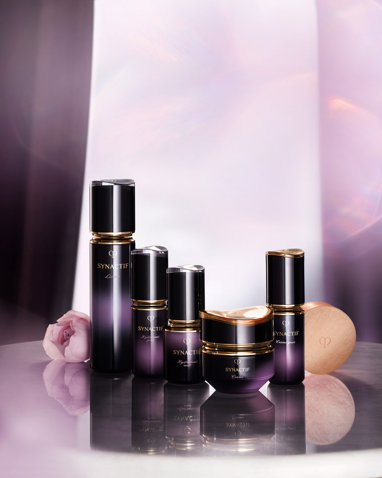 相片顯示Cl&eacute; de Peau Beaut&eacute; Synactif護膚系列產品，由左至右依序為：柔膚水、日間保濕乳液、晚間美容液、深層修護乳霜、極緻提升眼霜和護膚皂；全部採用黑色至紫色漸層包裝，點綴金色細節。