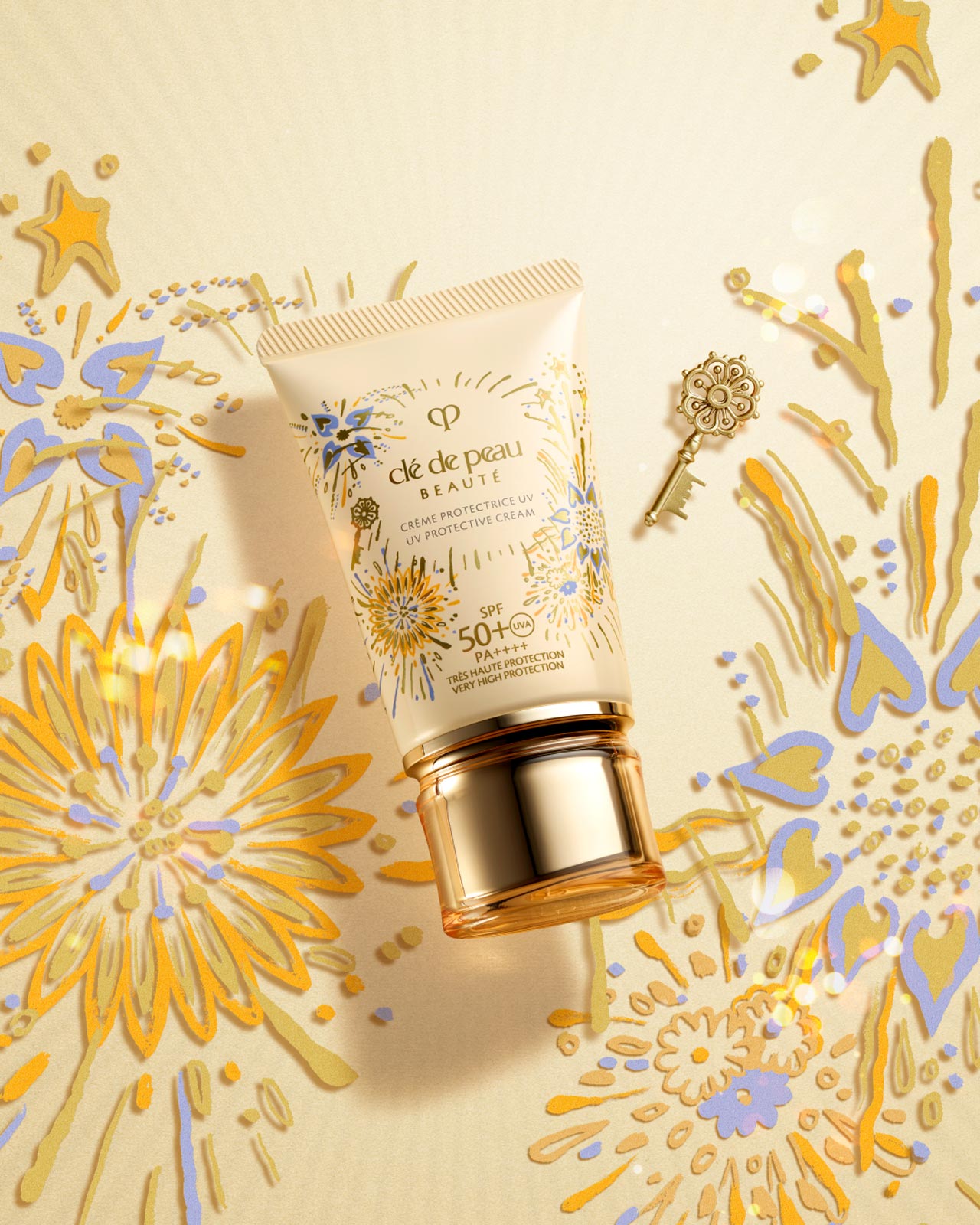 Photo of the LIMITED-EDITION UV PROTECTIVE CREAM. The light beige tube is adorned with gold, blue, and lavender fireworks motifs and a small gold key, with a gold cap. A vibrant fireworks pattern is in the background.