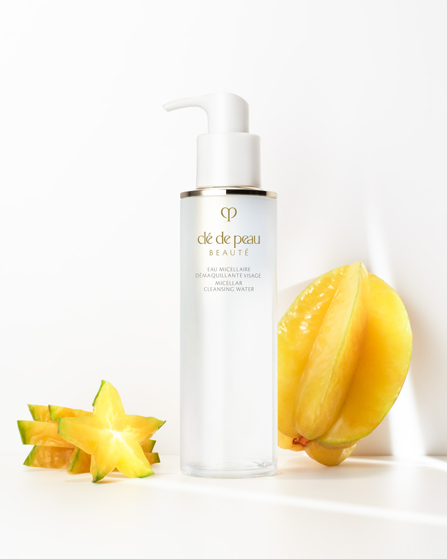 Photo of a bottle of Cl&eacute; de Peau Beaut&eacute; MICELLAR CLEANSING WATER placed beside a whole and sliced star fruit, highlighting the star fruit extract ingredient.