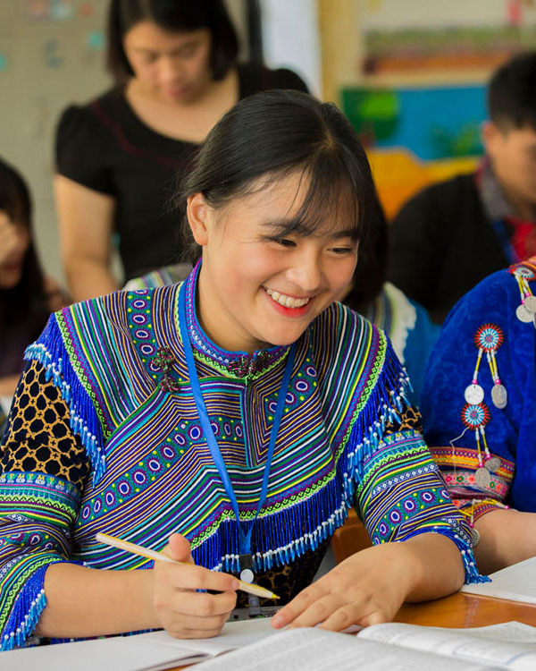 相片顯示一名女性穿著傳統服裝，在學習時展露笑容。