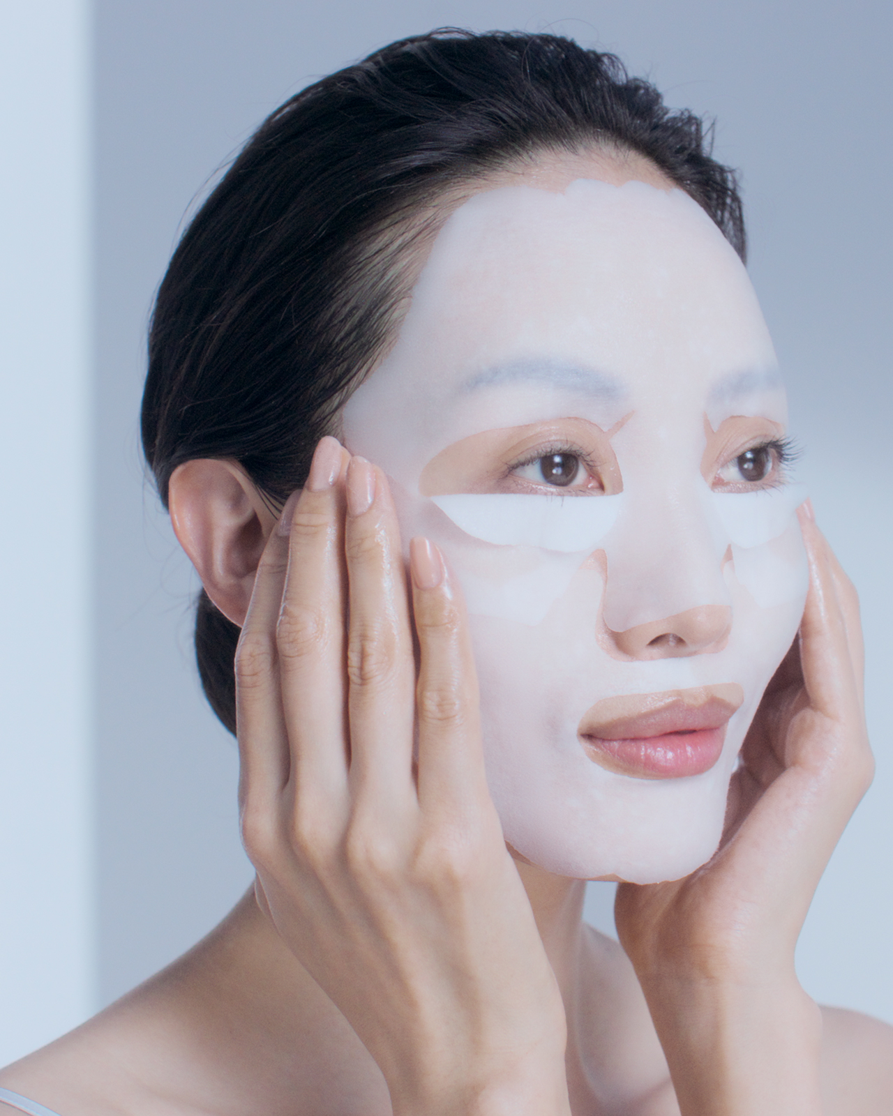 Photo of BRIGHTENING SERUM SUPREME and BRIGHTENING MASK TREATMENT SUPREME set.　Brightening serum in a clear bottle on the left, silver packets of exfoliating gel, lower face sheet mask, and upper face sheet mask on the right.