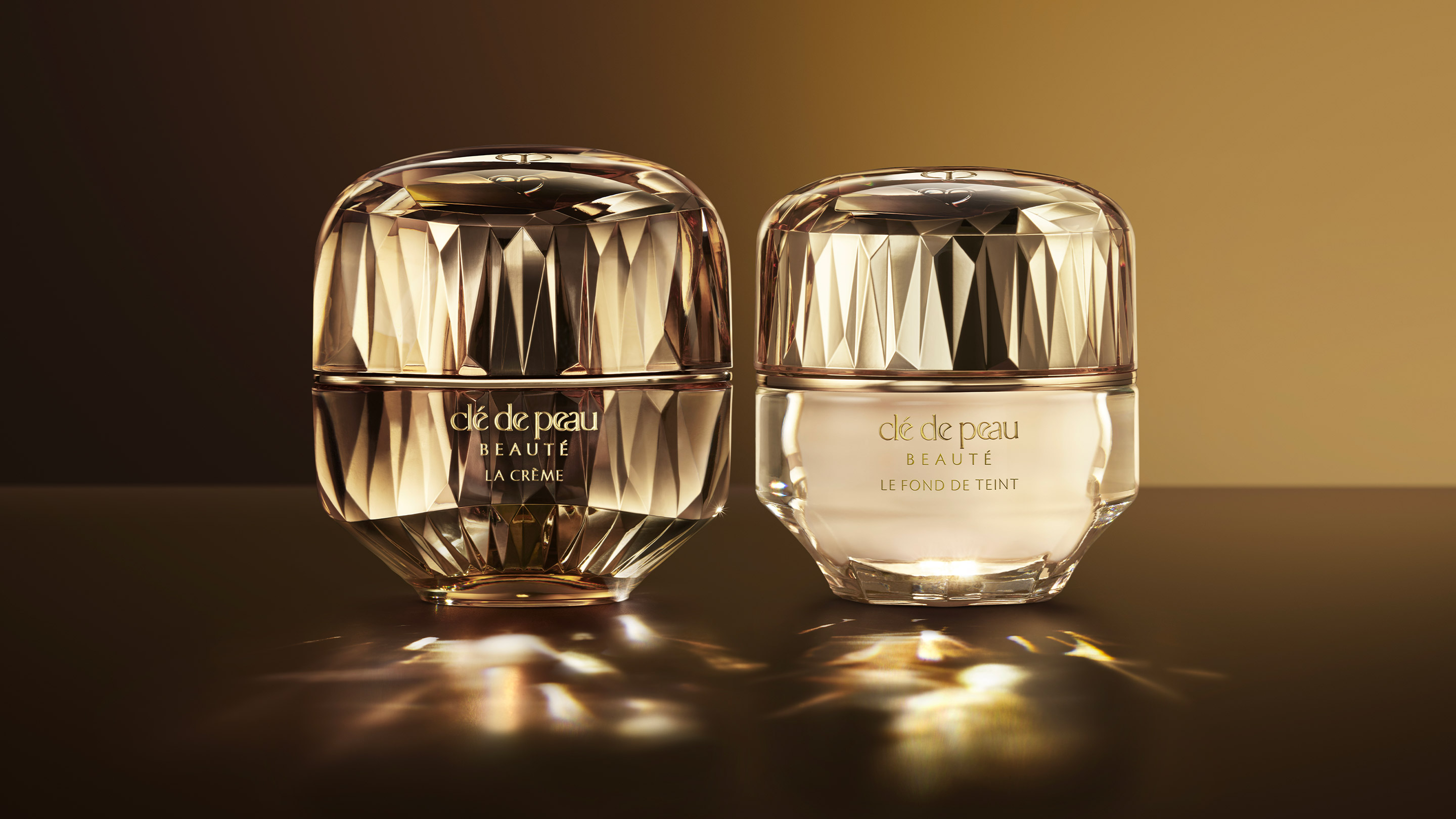 Photo of Cl&eacute; de Peau Beaut&eacute;'s legendary night cream, La Cr&egrave;me, and its luxurious foundation, The Foundation, shining elegantly on a dark, reflective surface.