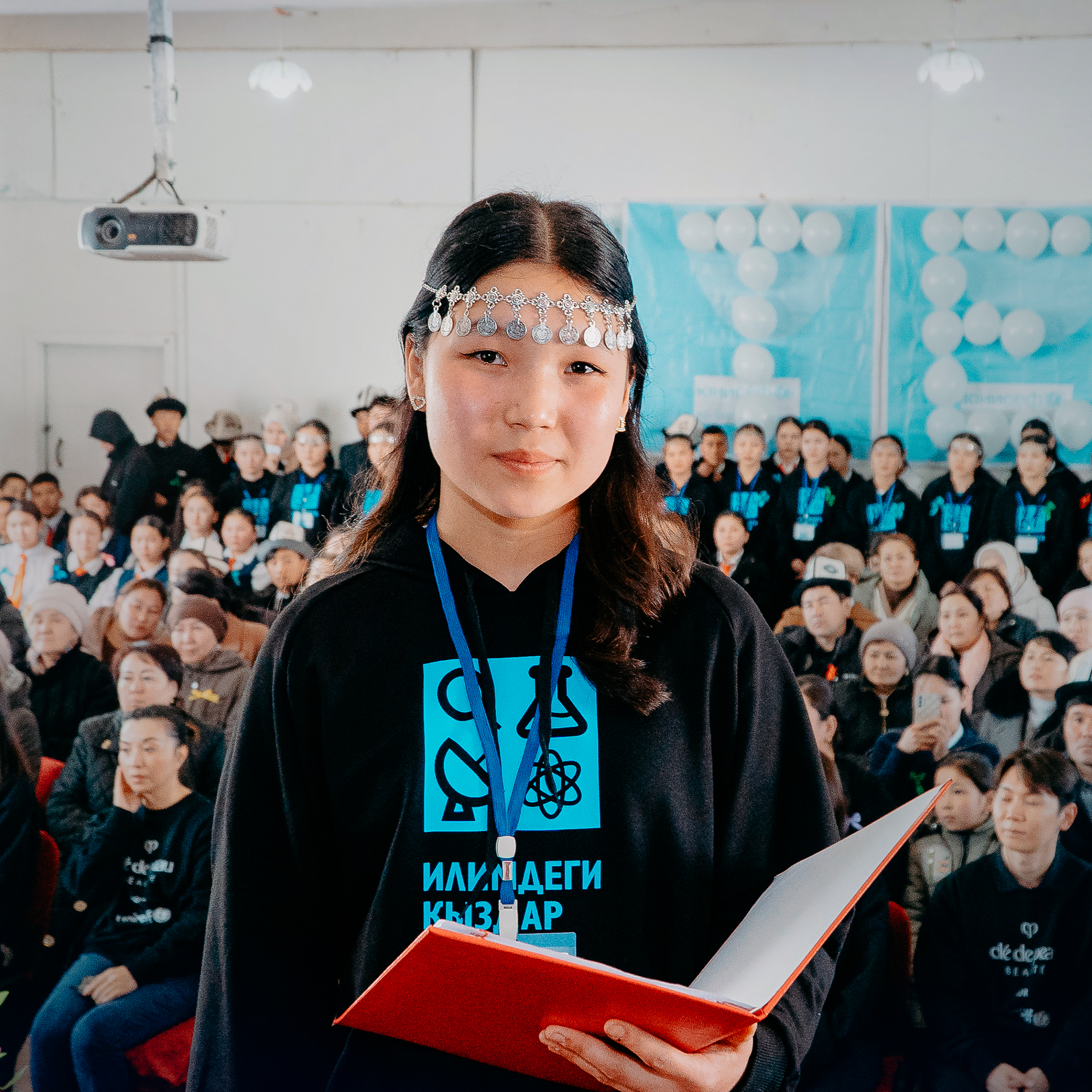  相片顯示一名吉爾吉斯女孩拿著紅色筆記本，於Cl&eacute; de Peau Beaut&eacute;的2025年UNICEF合作計劃訪問期間拍攝。