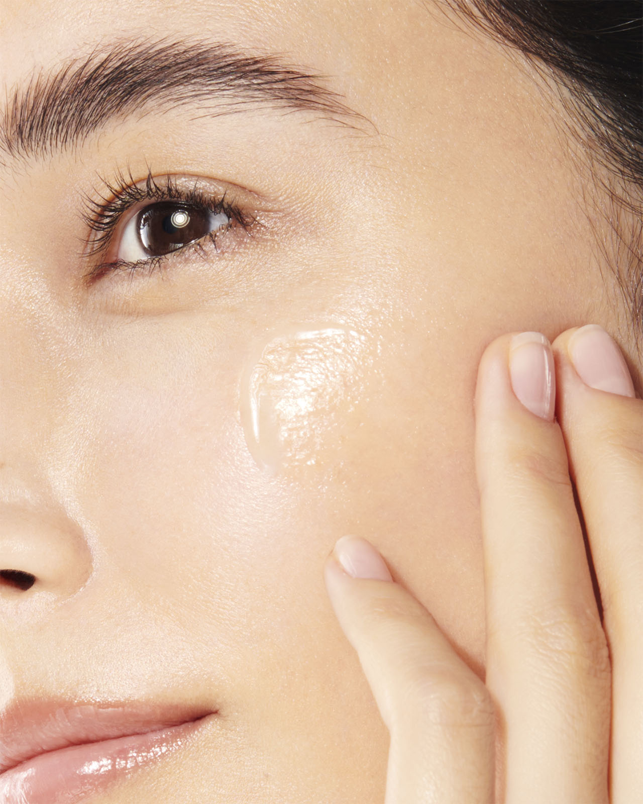 Photo of a close-up of a woman applying THE SERUM to her cheek.