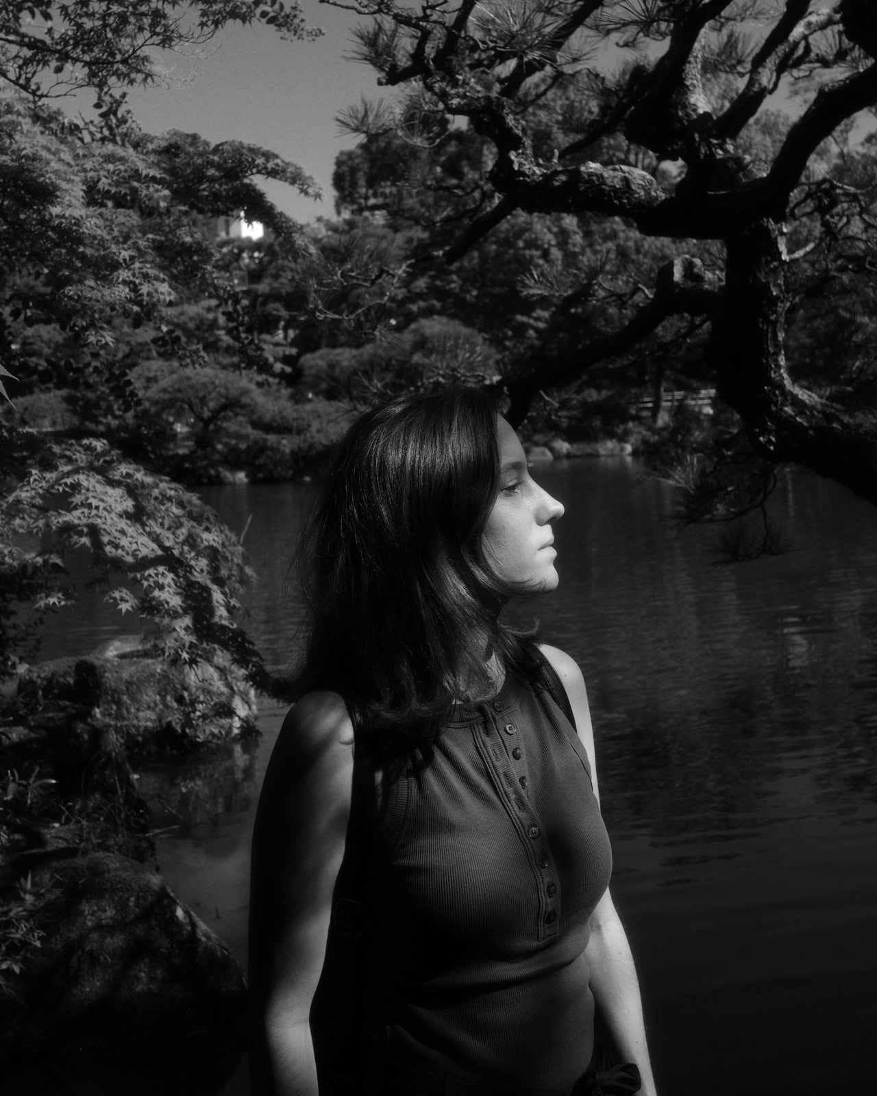  A black and white portrait of the artist, Lisa Zordan. Captured in profile, she stands by a pond in a serene Japanese garden, bathed in soft light that creates a thoughtful and tranquil atmosphere.