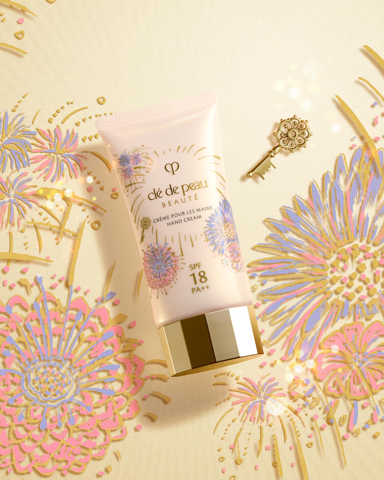 Photo of the LIMITED-EDITION BODY EMULSION . The light beige bottle is adorned with pink, blue, and gold fireworks motifs and a small gold key, with a gold cap. A vibrant fireworks pattern is in the background.