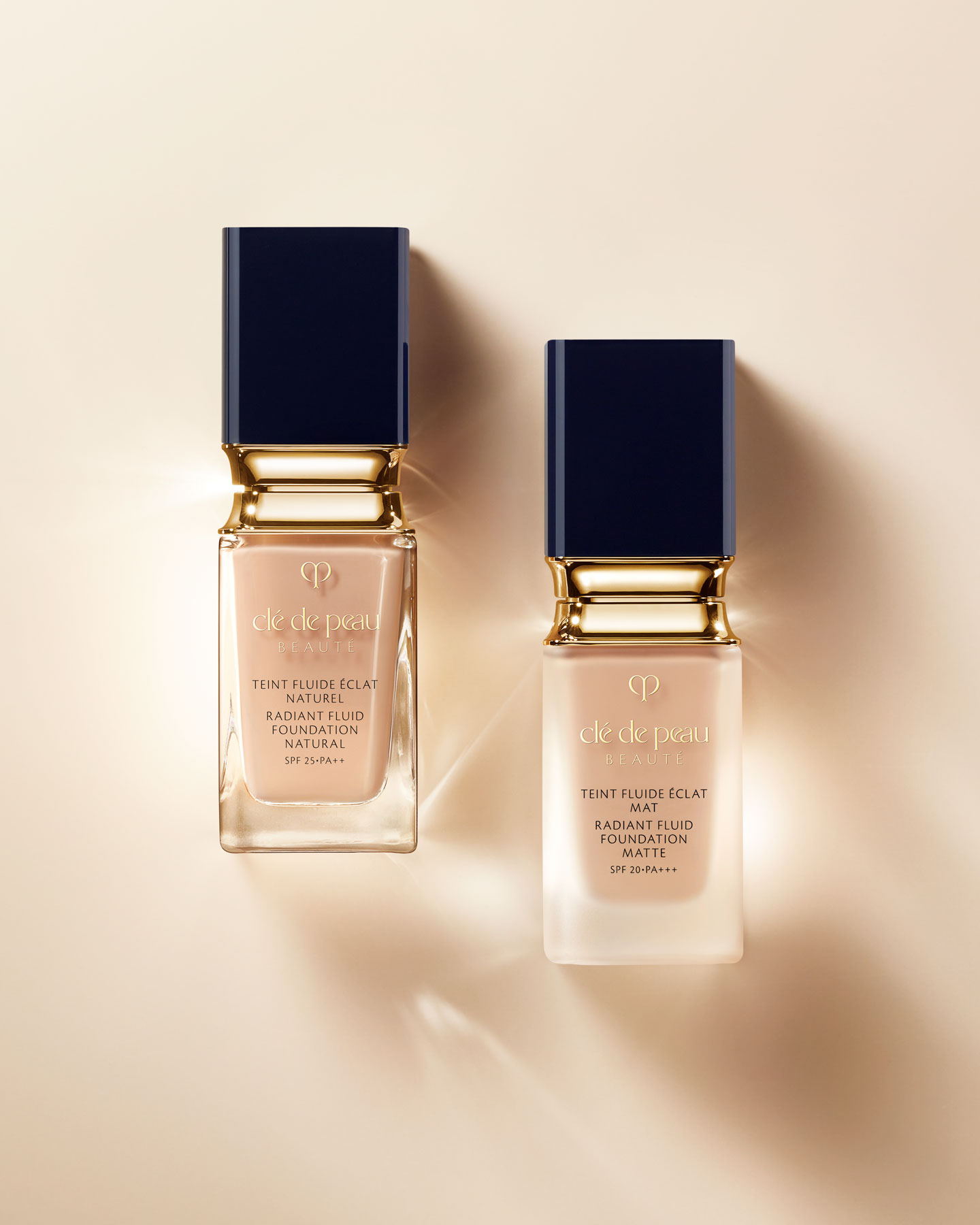 Photo of two foundation bottles with gold accents and blue-black caps; the left one is RADIANT FLUID FOUNDATION MATTE, and the right one is RADIANT FLUID FOUNDATION NATURAL.