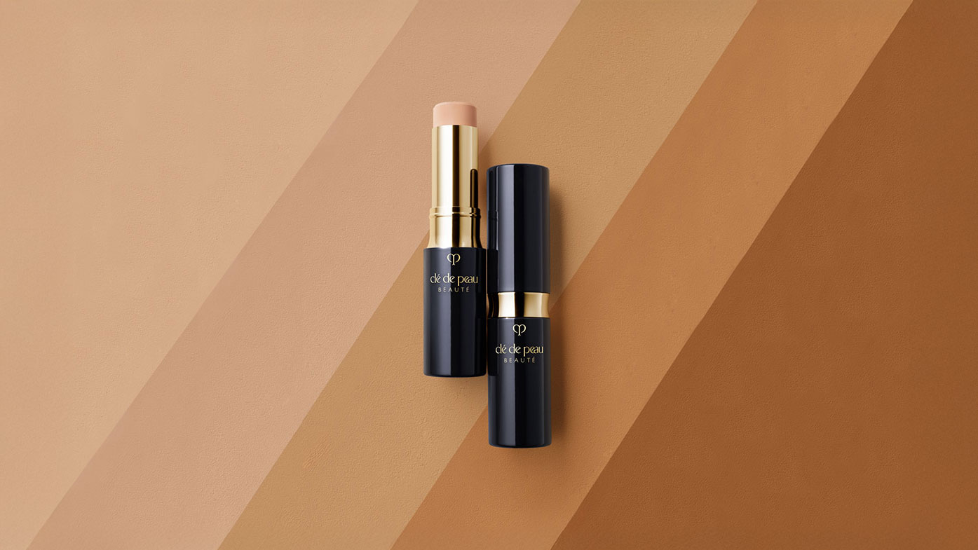 Photo of a stick concealer in a dark blue case with gold accents and the brand logo.