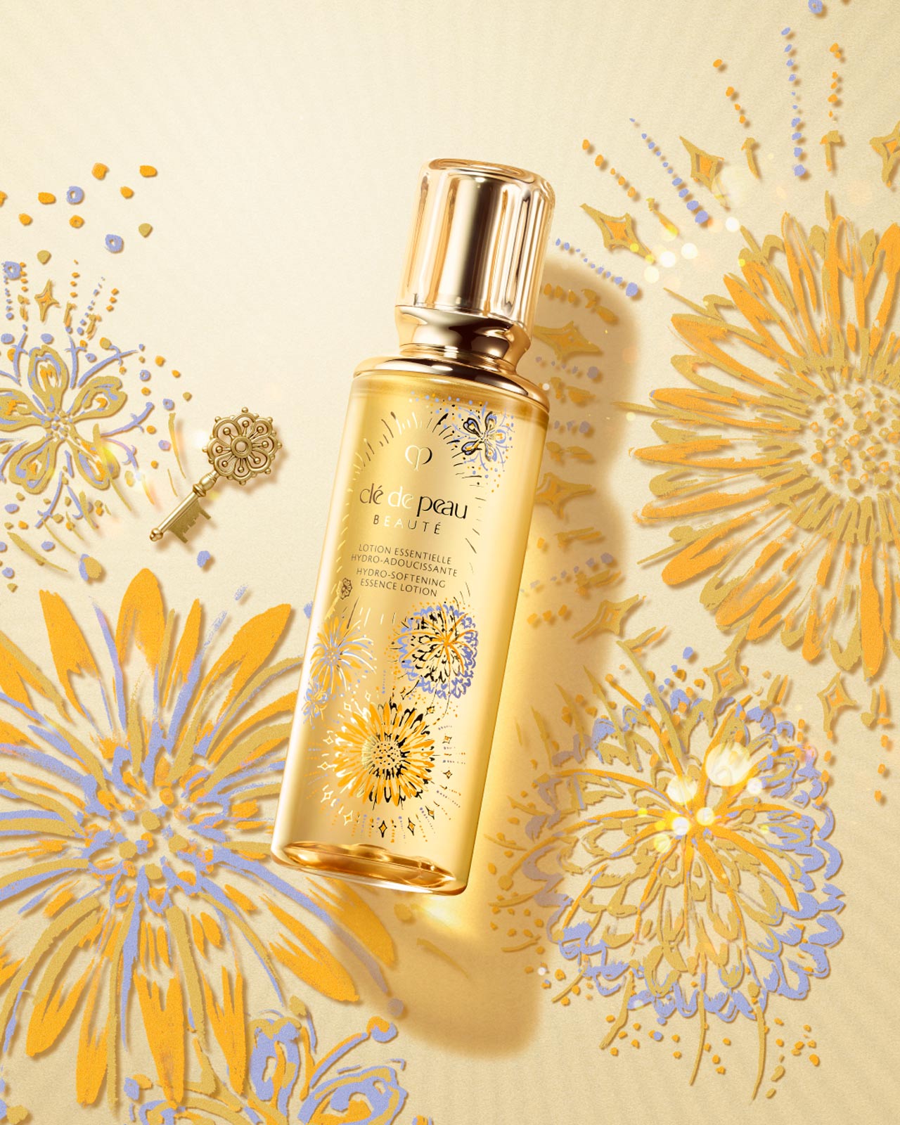 Photo of the LIMITED-EDITION HYDRO-SOFTENING ESSENCE LOTION. The golden-yellow bottle is adorned with gold, blue, and lavender fireworks motifs and a small gold key, reflecting the vibrant fireworks pattern in the background.