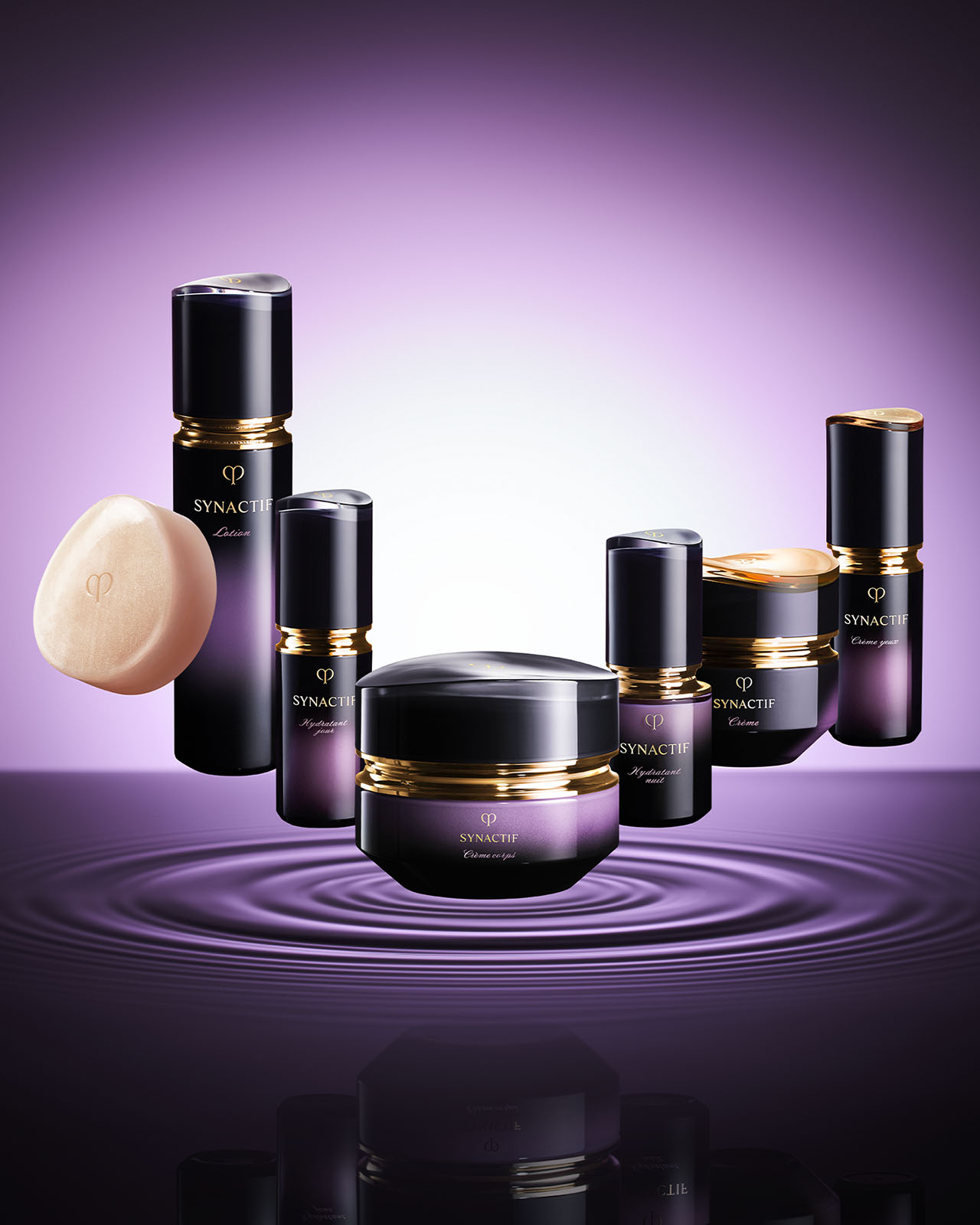 Photo of the full SYNACTIF skincare collection, including soap, lotion, and creams, floating above purple water ripples. The products feature deep violet gradients with gold accents against a soft purple background.