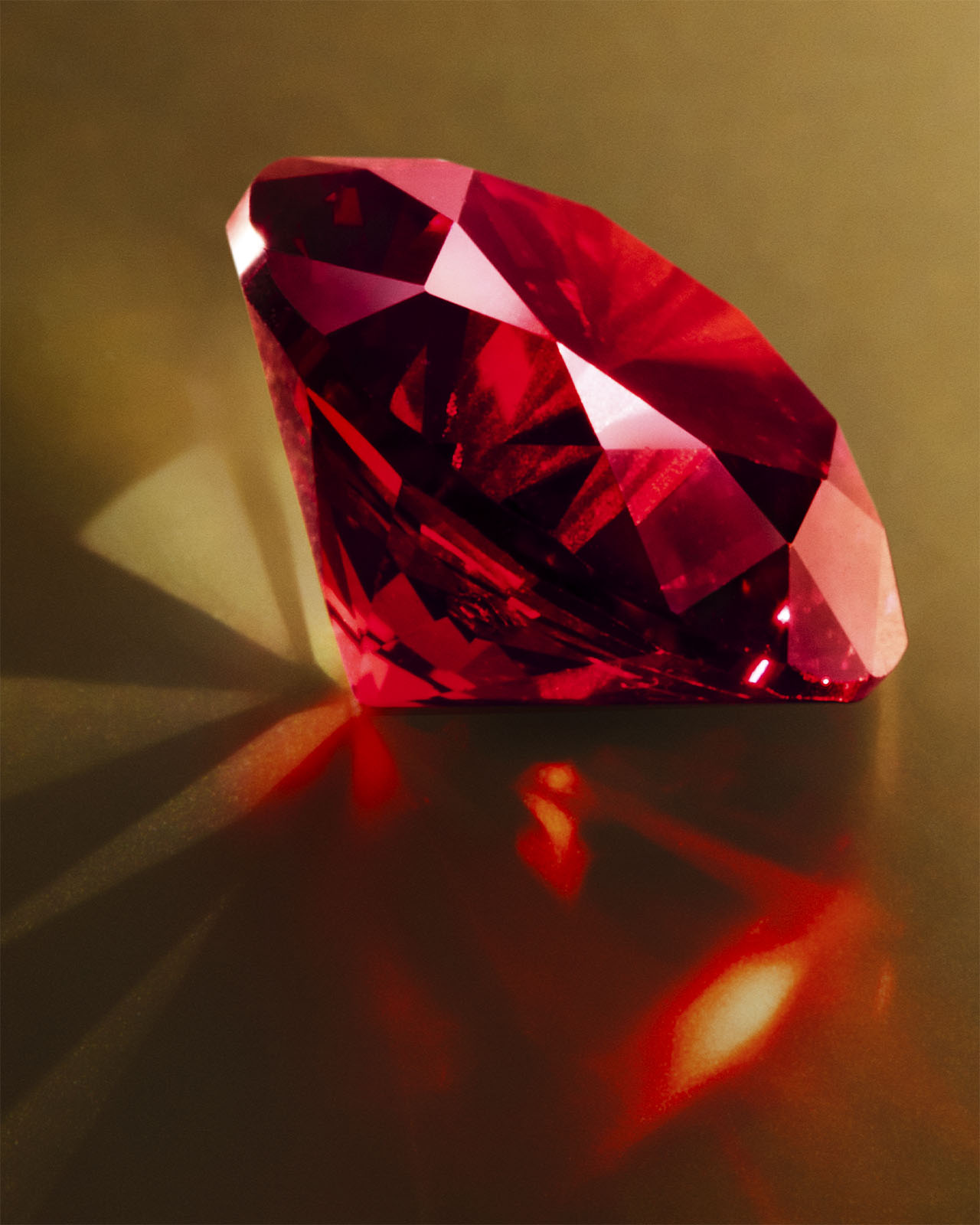 Photo of the red gemstone is placed under lighting. Reflections and shadows are visible.